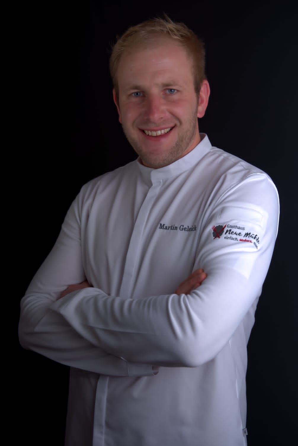 Martin Geleik, Chefkoch, Trägt weißes Koch Hemd, hat Arme verschränkt und lacht freundlich in die Kamera